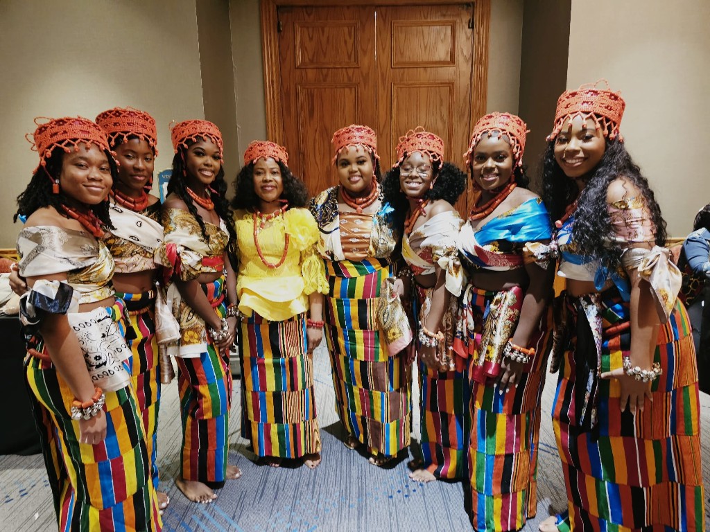 Children in traditional wrappers beside a feathered masquerade at an OFUSA celebration